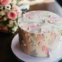 Okrągły tort z pastelowymi dekoracjami i bukietem róż w tle.