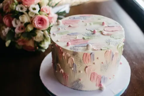 Okrągły tort z pastelowymi dekoracjami i bukietem róż w tle.