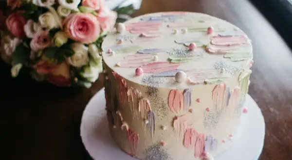 Okrągły tort z pastelowymi dekoracjami i bukietem róż w tle.