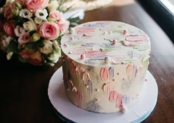 Okrągły tort z pastelowymi dekoracjami i bukietem róż w tle.